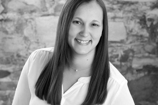 portrait of woman with long hair in white shirt in front of brick wall