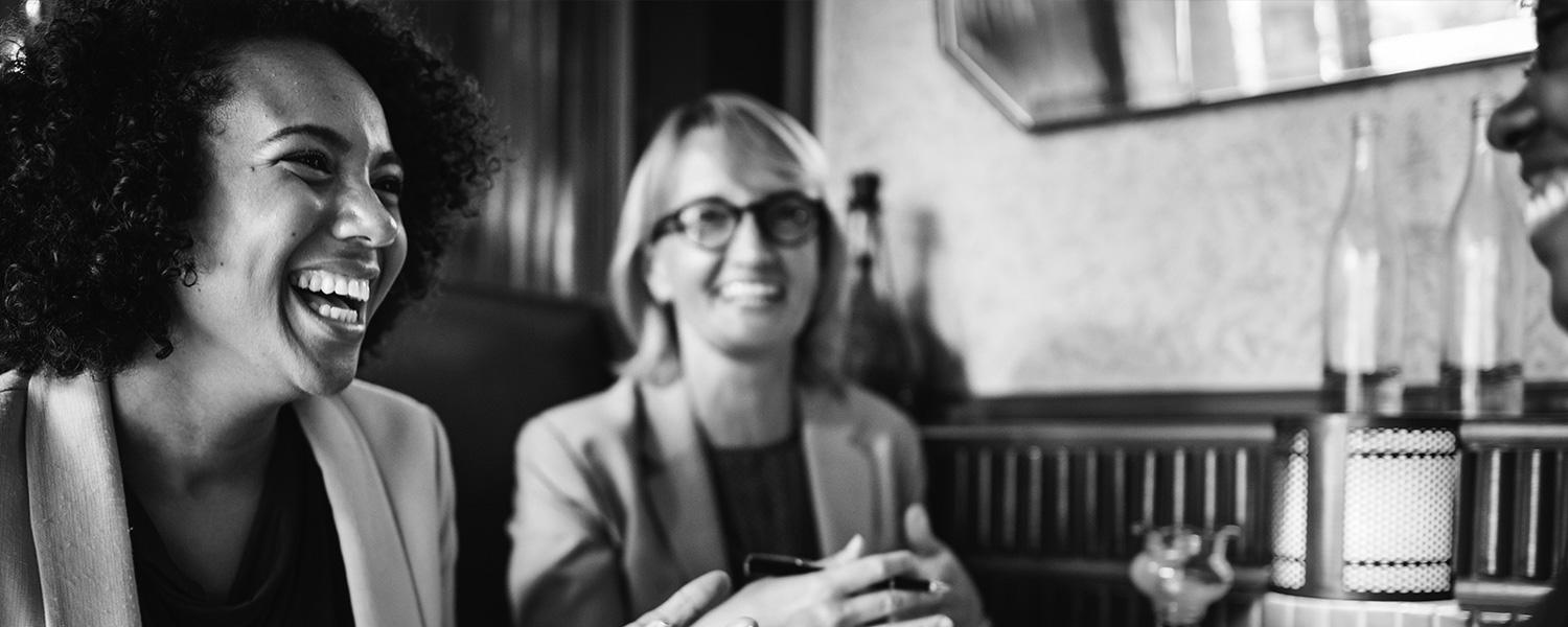 two smiling women sitting across from one woman in a booth