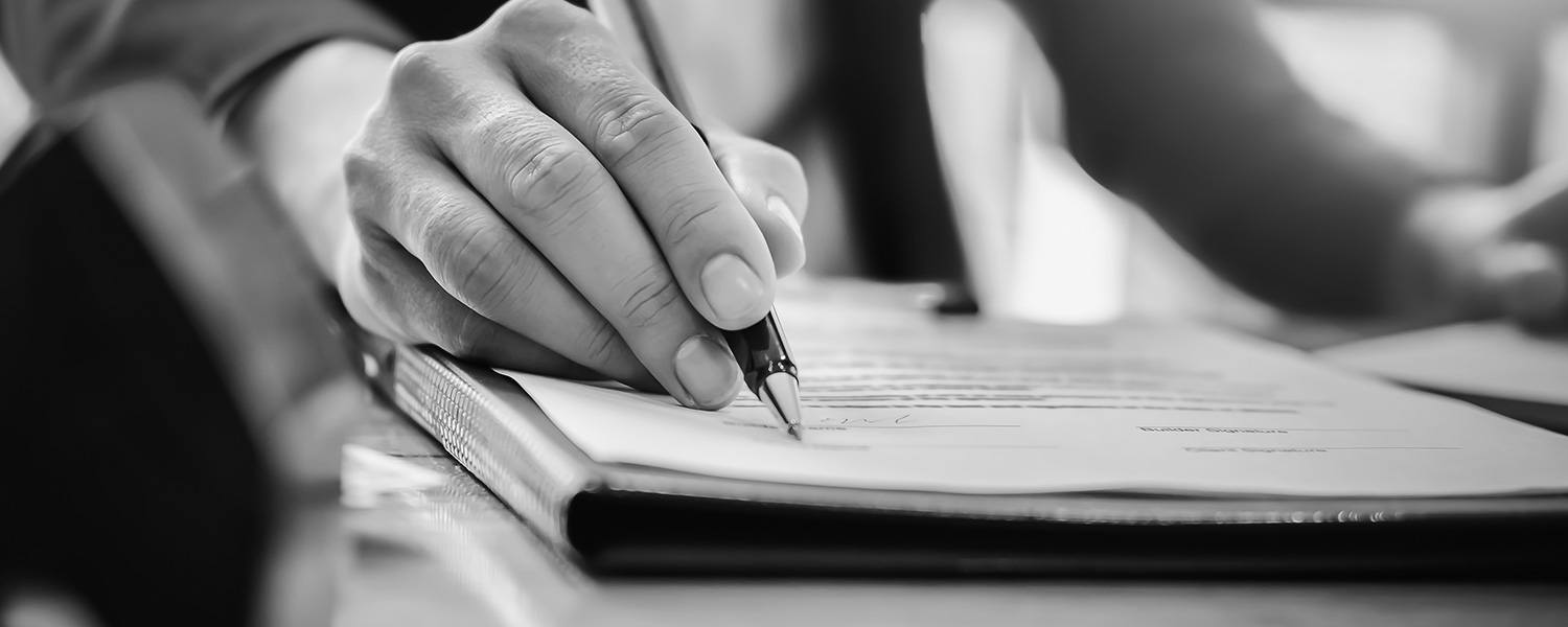 hand holding pen pointing towards signature area on paper
